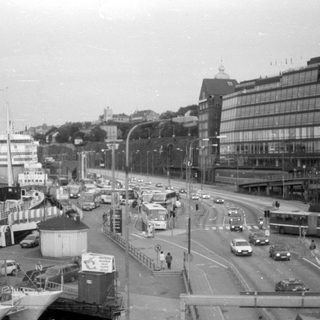 Waterfront road with traffic, ships, and modern architecture.