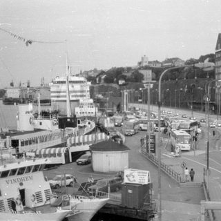 Waterfront road with traffic, ships, and modern architecture.