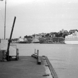 White cruise ship docked near a hillside town.