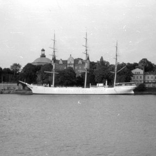 White three-masted sailing ship docked near domed building.