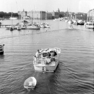 Motorboat towing a dinghy in a city harbor.