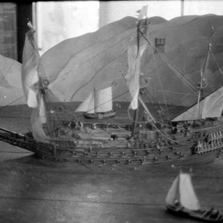 Model sailing ship against a stylized landscape background.