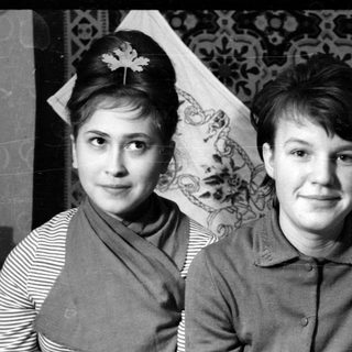 Two young women posing before patterned textiles.