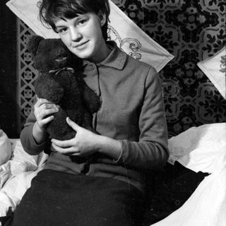 Person lying on a rug holding a teddy bear.