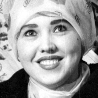 Person in headscarf against patterned textile background.