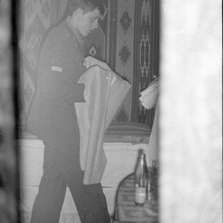 Man in military uniform holding fabric in a room.
