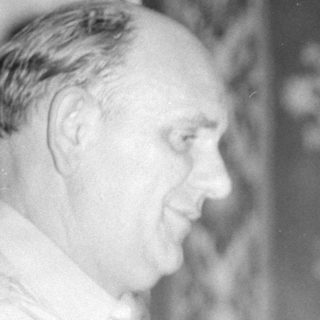 Two men indoors with a patterned wall hanging.