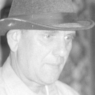 Man in a fedora in front of a rug.