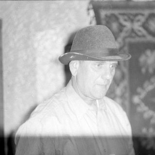 Man in a fedora in front of a rug.