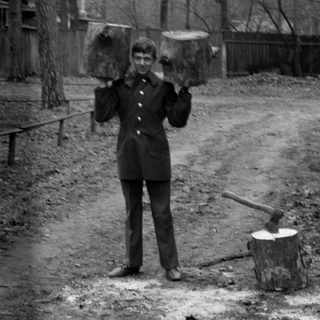 Man holding logs on shoulders next to an axe.