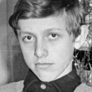 Young man seated beside a decorated Christmas tree.