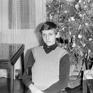 Young man seated beside a decorated Christmas tree.