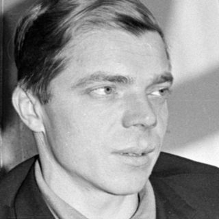 Man in a suit jacket against a plain wall.