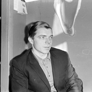 Man in a suit jacket against a plain wall.