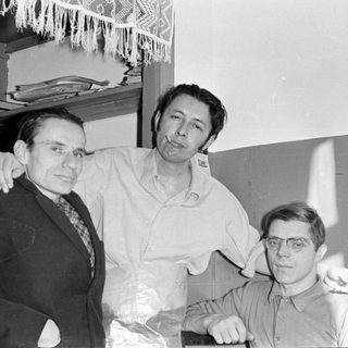 Three men posing indoors near a shelf.
