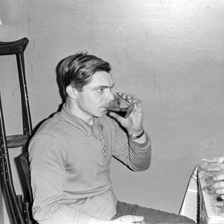 Man drinking from a glass next to a crutch.