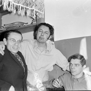 Three men posing indoors, two smoking cigarettes.