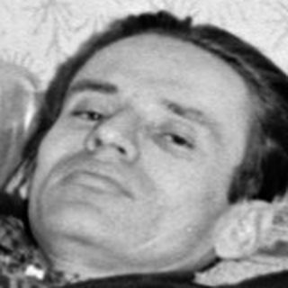 Man in a suit reclining on a patterned sofa.