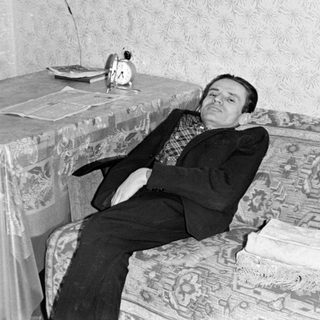 Man in a suit reclining on a patterned sofa.
