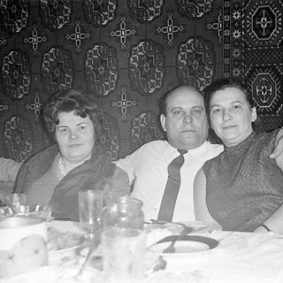 Three adults sitting at a table before a tapestry.